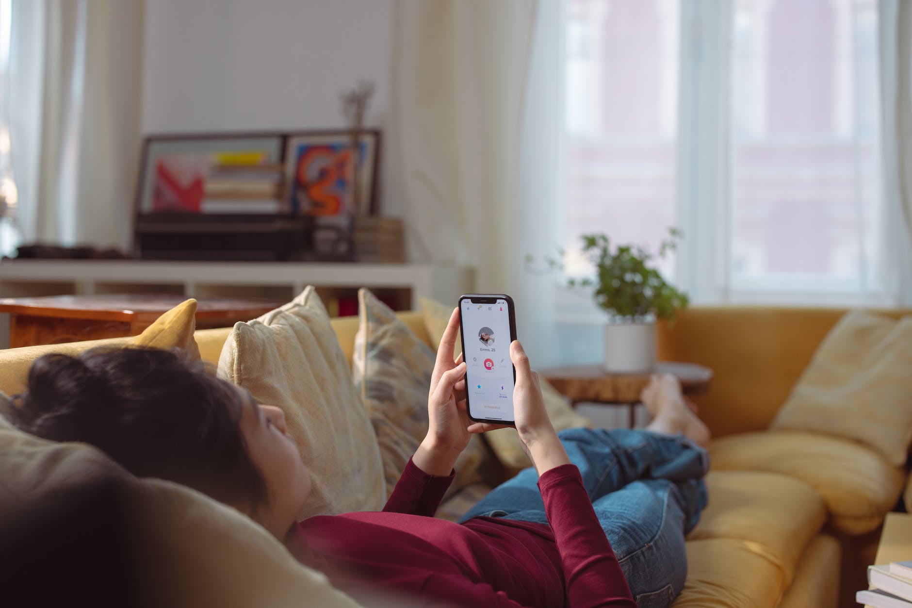 a person lying on sofa holding a smartphone with a person s profile on screen